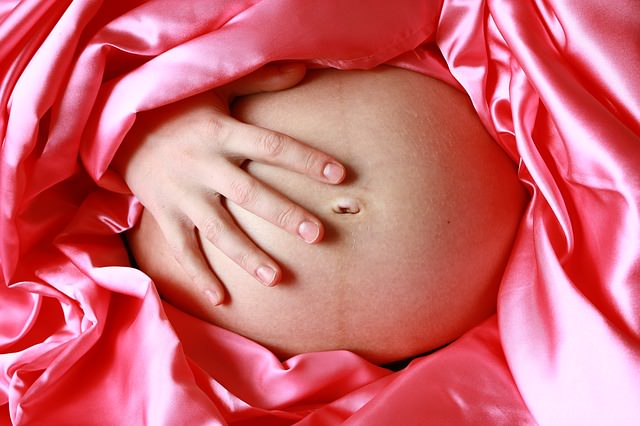 Kobieta w ciąży otoczona różową satyną trzyma rękę na brzuchu