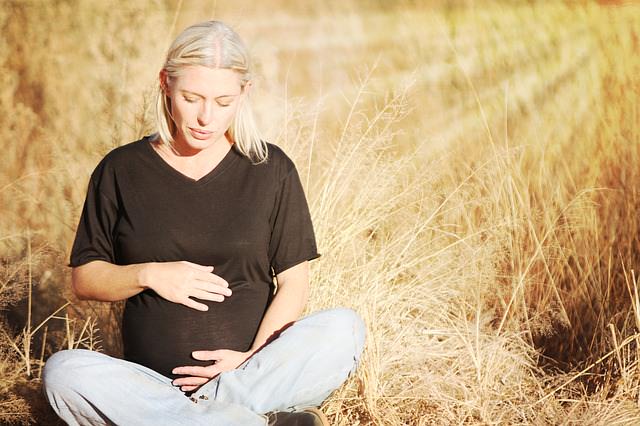 Kobieta w ciąży siedzi wśród łanów zbóż