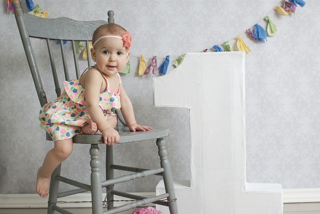 Dziecko w kolorowej sukience na krześle, obok wiszą kolorowe ozdoby