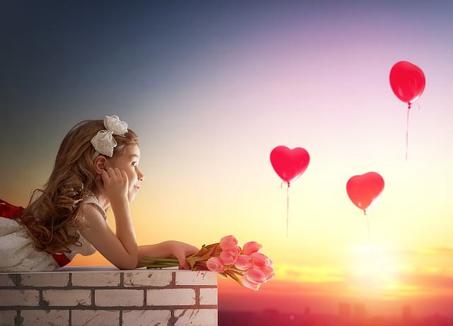 Dziewczynka na murku, w powietrzu baloniki z serduszkami